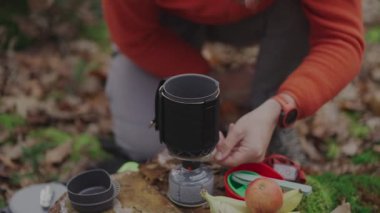 Hiker twists power control switch and ignites gas burner with spark by pressing piezo spark button on handheld cooking system for a camping trip in the fall. Cooking equipment for the expedition. 