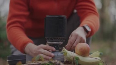 Hiker twists power control switch and ignites gas burner with spark by pressing piezo spark button on handheld cooking system for a camping trip in the fall. Cooking equipment for the expedition. 