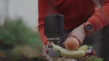 Traveler prepares to eat camping meals and fires up spark button gas stove in portable camping cooking system to boil water in woods in autumn. Inventory for cooking. Hiker igniting camping stove. 