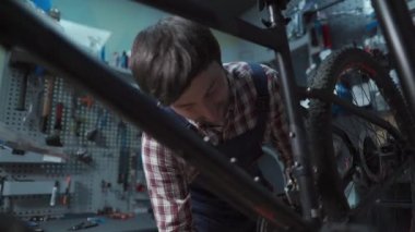 Theme of repair and tuning of bicycles. Caucasian male bicycle mechanic repairing transmission on bike on rack in shop. The repairman twists the bicycle crankset and bottom bracket with a tool. 