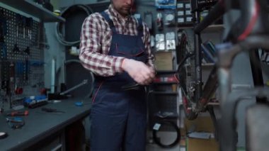 Repairs bicycles in protective clothing at workplace in mechanics repair shop. Bicycle technician adjusts and sets crank on cycle. The crank set and bike carriage. Bicycle renovation profession. 