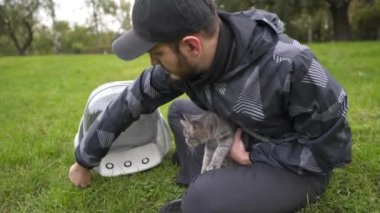Having time outdoors with domestic cat. House cat carried to garden in animal carrier, transparent bag transfer feline. Owner stroking cat in nature. Bubble backpack animal carrier, traveling with pet