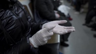 Senior Caucasian woman in subway room, wearing white medical gloves and protective mask on face, conducts an antiseptic treatment of hands after trip public transport during coronavirus quarantine.