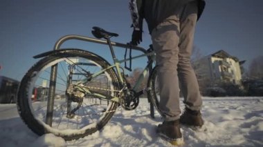 Male cyclist unlocks parked bicycle in street parking lot in snowy, freezing winter weather in Germany. Opening a cycle lock. Protecting bike from being stolen. Man is unlocking bike on rack outside. 