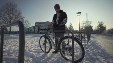Male cyclist unlocks parked bicycle in street parking lot in snowy, freezing winter weather in Germany. Opening a cycle lock. Protecting bike from being stolen. Man is unlocking bike on rack outside. 