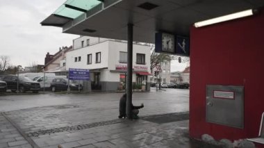 November 20, 2022. Munich, Germany. Beggar sits on ground asking for money near the entrance to subway and commuter train at Trudering station in Munchen in cold fall weather. Homeless asks for cash. 