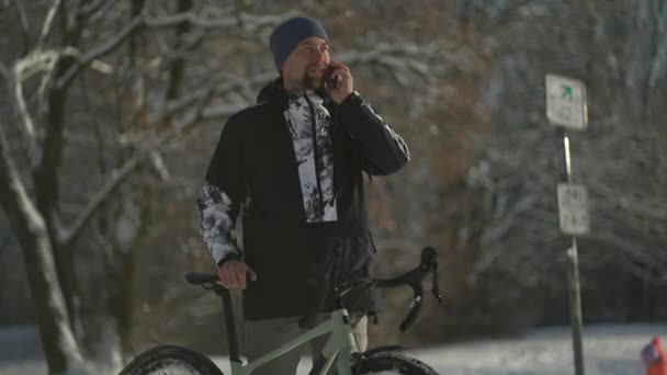 ドイツの雪に覆われた晴れた冬の天候のサイクルトレイル上の自転車から携帯電話で話す男の自転車乗り 冬は森の中でサイクリング 自転車で通勤しています 環境に優しい — ストック動画