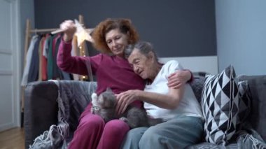 Emekli yaşlı insanlar ve hayvanların evcil hayvanları. Evcil, oynak bir hayvan, yaşlı bir anne ve yaşlı bir kız. Kedi terapisi. Tekir gri İskoç Heteroseksüel kedi halatla ve aileyle oyuncak yakalar..
