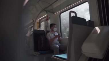 Tourist on passenger train in Germany using a smartphone application, wearing protective mask. Railroad passenger holding a mobile phone during a journey on a train with a KN95 FFP2 protective mask. 