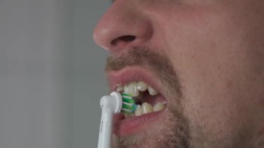 Man brushes his teeth with an electrical tootbrush at morning bathroom before work. Male uses an electric sonic dental cleaning brush. Daily dental hygiene and oral health with eletrical teethbrush. 