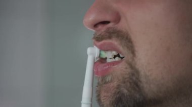 Man brushes his teeth with an electrical tootbrush at morning bathroom before work. Male uses an electric sonic dental cleaning brush. Daily dental hygiene and oral health with eletrical teethbrush. 