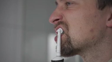 Theme of brushing and whitening teeth with a modern electric toothbrush. Close-up of a man cleaning his teeth with an ultrasonic dental brush. Morning routine, oral hygiene. Oscillating toothbrush. 