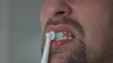Close-up of man cleaning teeth by an ultrasonic toothbrush. Male brushing his teeth with electric teethbrush. Theme oral health and dental hygiene. Morning sanitation procedures in the bathroom. 