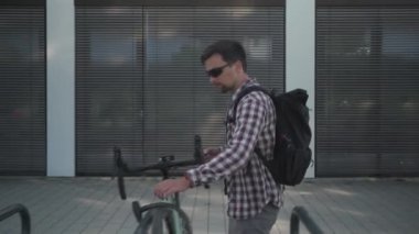 Security and anti-theft lock for bicycle. Male cyclist unlocks cycle in outdoor parking lot in city in Europe. Guy unbuckles bike in public parking space and rides away. Protecting bike from stolen. 