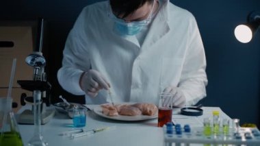 Scientist from food testing laboratory tests food for infection, chemical and Genetically Modified Organisms GMO by applying a red liquid with a pipette to chicken breast for chemical reactions. 