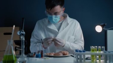 Scientist dripping red liquid on cultured meat, waiting for reaction in laboratory. Microbiologist examines meat sample by dispensing colored liquids from chemical beakers use laboratory pipettes. 