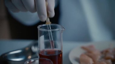 Genetics laboratory technician takes red liquid from a glass vial with pipette and applies it to chicken fillet. GMO test laboratory. Genetically modified meat. DNA. Nutrition expert testing food. 