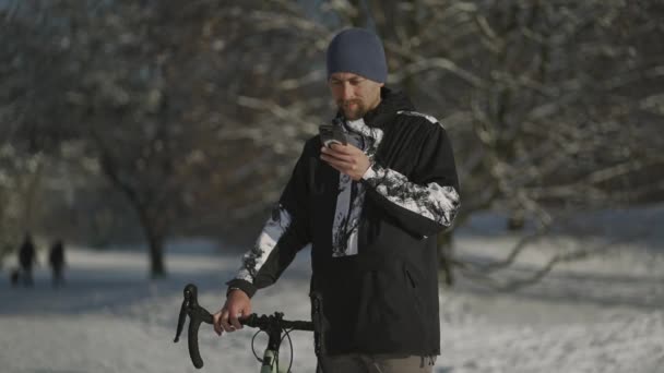 サイクリストは道路を見つけるためにスマートフォンを使用しています 地図上のルートを構築します 雪の中で冬のナビゲーション ドイツの晴れた天気 スポーツ アクティブライフスタイルと現代技術 電話でのGpsナビゲーション — ストック動画