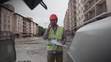 İnşaat alanındaki miğferli müfettiş inşaat belgeleriyle kaliteyi kontrol ediyor ve apartman blokları inşa etmeyi planlıyor. İnşaat işlerinin yanındaki makineler apartman sitesinde telefonla konuşuyorlar. 