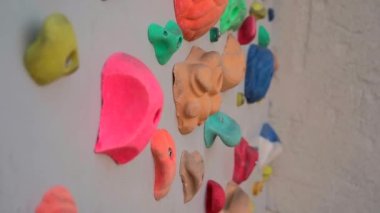 Boulding Center 'da tutunarak duvara tırmanıyor. Boş bir kaya tırmanma salonunun duvarı. Yapay taşlı kaya uçurumu. Çocuklar renkli tutacakları ve yol işaretleriyle duvarlara tırmanıyor.. 