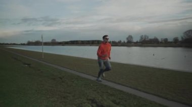 Almanya, Münih 'te sonbaharda Park Gölü' nün yanında koşan spor giyimli genç bir adam. Sağlıklı bir açık hava yaşam tarzı için egzersiz. Erkek sonbaharda gölet boyunca koşuyor. Kros hakkında eğitim oturumları suyla yapılıyor. 