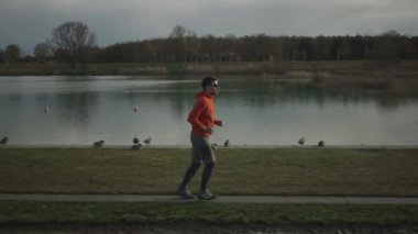 Almanya, Münih ve Almanya 'da sonbaharda parkta yürüyüş yolu boyunca koşan sporcu bir adam. Sonbaharda bir göletin yanında koşan bir erkek. Suyun yanında açık hava egzersizi. İnsanlar ve spor konsepti. 