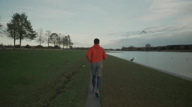 Almanya 'da parkta göl boyunca koşan bir adam. Atletik genç insan doğada koşar. Sağlıklı bir yaşam tarzı. Erkek, Münih 'teki bir şehir parkında gölet kenarında koşuyor. Göl kenarındaki patikada koşan adam.. 