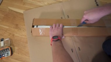 Adam yerde toplanmak için üzerinde bıçak olan karton parçaları buldu. Ev mobilyası montajı tek başına. Beyazlı kutu, mobilyaları kendin yap. Alıcı, kurulmaya hazır katlama tablosunu toplar