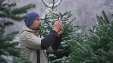 Erkek web blogcusu, sosyal medya ağları için kameralı telefon ve kışın bir Noel pazarında köknar ağacı seçmekle ilgili online yayın hizmetleri üzerinden takipçileri kullanarak video çekiyor.. 
