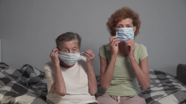 Dwie Starsze Kobiety Zakładają Maski Medyczne Patrząc Kamerę Siedzącą Łóżku — Wideo stockowe