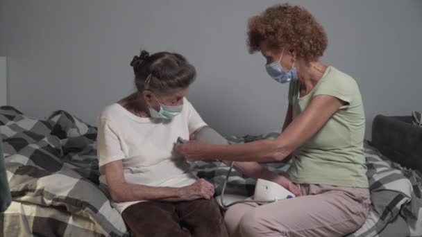 一名戴口罩的成熟女性在禽流感爆发和流感爆发期间测量老年女性的血压 护理者对病人使用电子血压计 血压计 — 图库视频影像