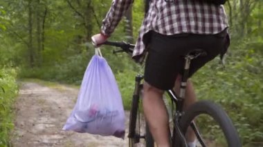 Bisikletle gidiyor. Bağış gönüllüleri, çöp torbasında orman enkazı ve plastik atık ve bisiklet gidonunda nakliye araçları topluyor. Çevre koruma, doğada toparlanma. Kirlilik. Ekolojik sorun.