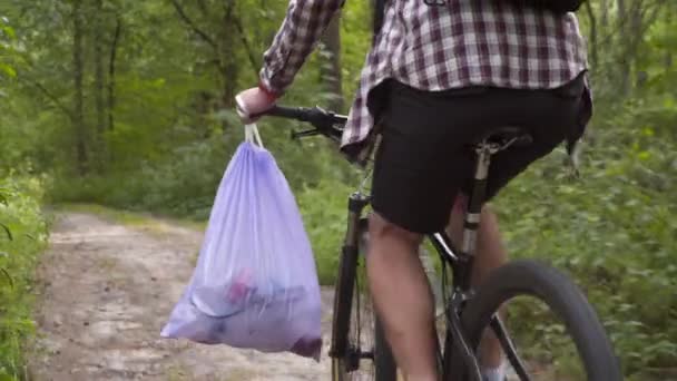 骑自行车打柴 慈善志愿者在垃圾袋中收集森林垃圾和塑料废物 并用自行车的把手运送 生态保护 在大自然中拾起 生态问题 — 图库视频影像