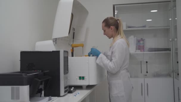 戴防护手套的诊断实验室科学家与生化自动血液分析仪一起工作 实验室技术人员将血液样本装入机器人血液分析仪 医疗设备 — 图库视频影像