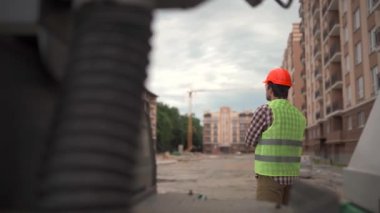 Tema mimarisi ve inşaat mühendisliği. İnşaat alanında çalışan genç bir erkek müfettiş kameraların önünde duruyor ve iş günü sonunda işçilerin olmadığı konut alanlarını denetliyor.. 