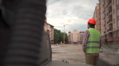 Turuncu şapkalı ve üniformalı bir inşaat işçisinin iş saatinin sonunda bir apartmanın şantiyesine baktığını gördüm. Tema mimarisi ve inşaat mühendisliği. 