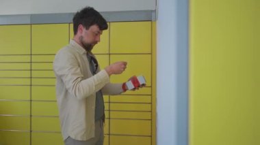 Paketi bırakmak için otomatik teslimat terminalini kullanan bir erkek müşteri. Posta otomatik paket alma noktası adamı işletim ekranında telefon ve kutu tutuyor.. 