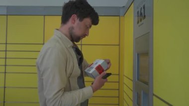 Paketi bırakmak için otomatik teslimat terminalini kullanan bir erkek müşteri. Posta otomatik paket alma noktası adamı işletim ekranında telefon ve kutu tutuyor.. 