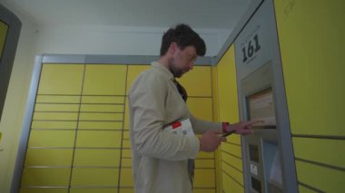 Paketi bırakmak için otomatik teslimat terminalini kullanan bir erkek müşteri. Posta otomatik paket alma noktası adamı işletim ekranında telefon ve kutu tutuyor.. 