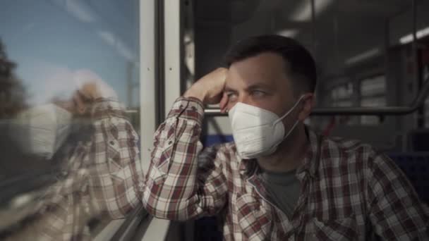 ドイツの郊外の電車の窓のそばに座っているマスクの悲しい 疲れた男 ドイツ鉄道の旅客列車 流行とパンデミックの間に旅行する 鉄道の公共交通機関で安全に旅行する — ストック動画