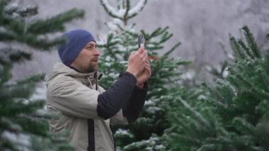Erkek web blogcusu, sosyal medya ağları için kameralı telefon ve kışın bir Noel pazarında köknar ağacı seçmekle ilgili online yayın hizmetleri üzerinden takipçileri kullanarak video çekiyor.. 