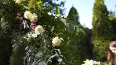 Profesyonel çiçekçi düğün kaydı için festival kemerini dekore ediyor. Kadın düğün dekoru kuruyor. Dekoratör, açık hava düğün törenini çiçekler ve yeşilliklerle süslüyor..