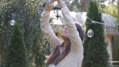 Kadın dekoratör bahçede yapılacak düğün törenleri için siyah tel çelenkler hazırlıyor. Kadın tasarımcı açık hava ışığını düğün töreni için hazırlıyor. Düğün kemerinde çiçekler ve lambalar ile dekorasyon. 