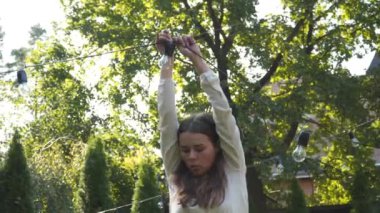 Kadın dekoratör bahçede yapılacak düğün törenleri için siyah tel çelenkler hazırlıyor. Kadın tasarımcı açık hava ışığını düğün töreni için hazırlıyor. Düğün kemerinde çiçekler ve lambalar ile dekorasyon. 