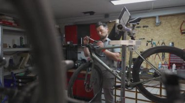 Bisiklet teknisyeni bisiklet sapını ve gidonu özel aletle büküyor. Tamirci demir cıvataları takmak için alet kullanıyor. Bisiklet servisi. İş yerinde motor tamircisi. Tamir döngüleri. Atölye. Bisikletlerin tamiri. 