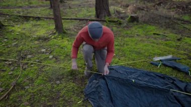 Tourist makes camp in woods, sets up tent in meadow in fall forest, prepares for an overnight stay in campsite. Backpacker builds tent on solo autumn trip in forest. Hiking and staying in nature. 
