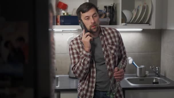 酔った男は手にアルコールの未完成のボトルで立っており 夜遅くに台所で自宅で電話をかけます アルコール依存症とうつ病の概念 酒を飲んでる 社会問題 — ストック動画