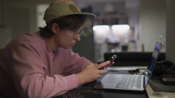 Kobieta Czapce Okularach Różowym Pulowerze Siedzi Laptopem Wieczorem Używa Smartfona — Wideo stockowe