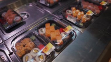 Maskeli adam süpermarkette raftaki plastik kutuda suşi seçiyor. Japon yemeği siparişi. Maske yok, giriş yok. Tek kullanımlık plastik konteynırda sağlıklı yiyecekler. Suşi ile beslenme çantası..