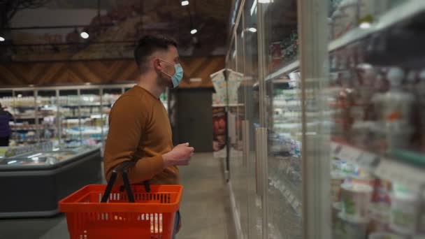 男人在商店里挑选日用品 提着购物篮散步 在超市里检疫时购买必需品 戴防护口罩 新的正常 Covid 19和购买 不准戴面具不准入内 — 图库视频影像
